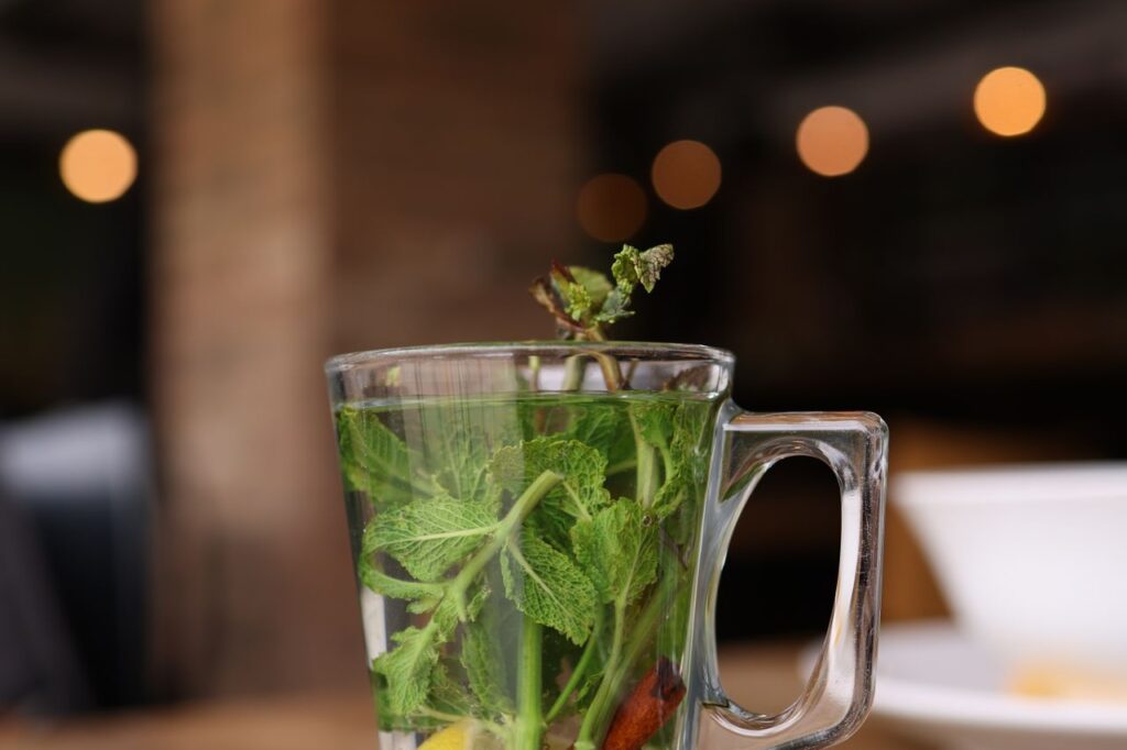 Glass mug of fresh peppermint tea with a sprig of mint and lemon on a saucer in a warmly lit café