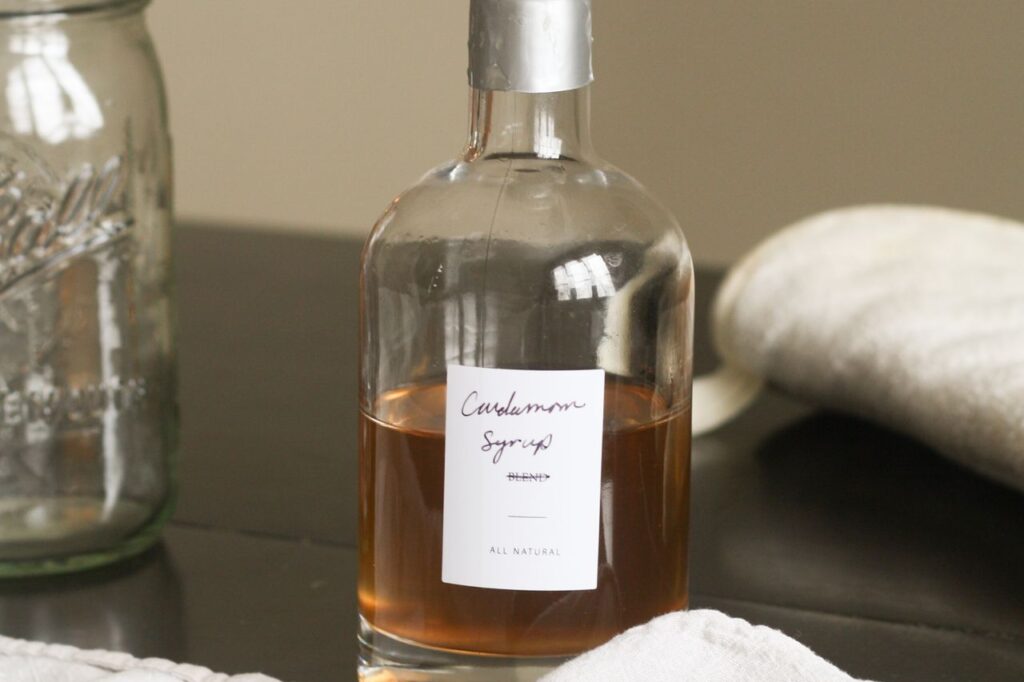 Finished homemade syrup in a labelled glass bottle next to an empty mason jar and lids on a kitchen counter