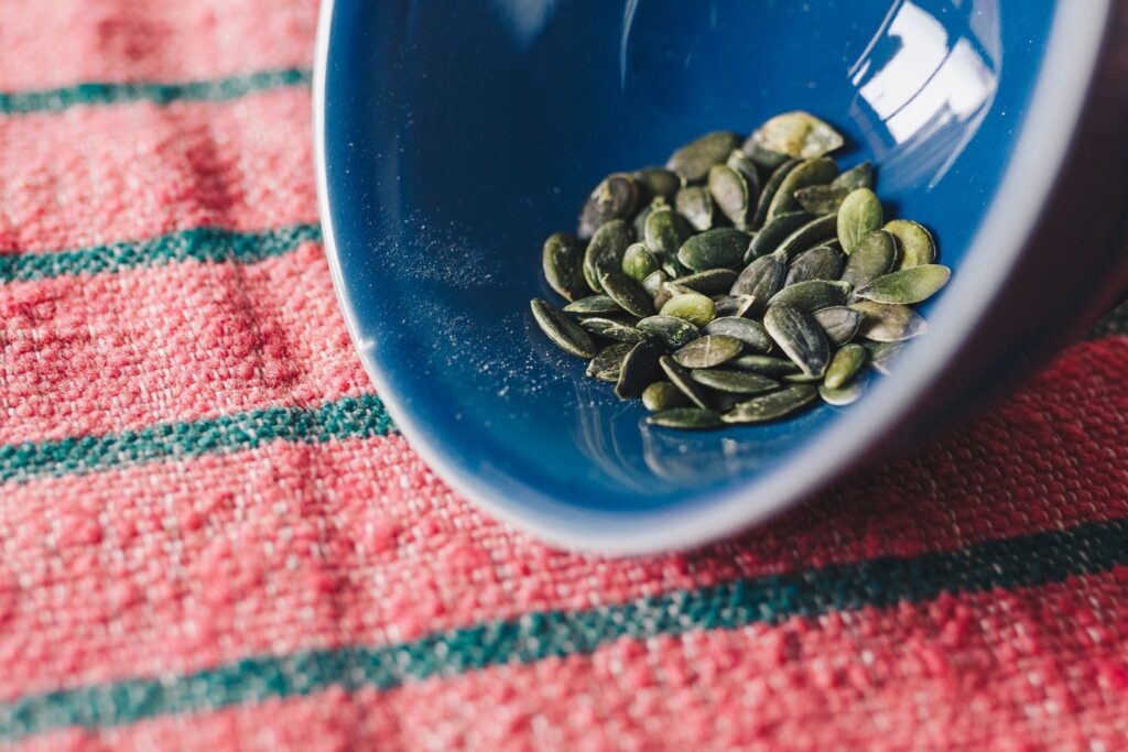 Green pumpkin seeds in a blue bowl on a striped cloth