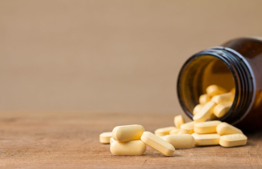 Yellow capsules spilling from an open brown glass supplement bottle onto a wooden surface