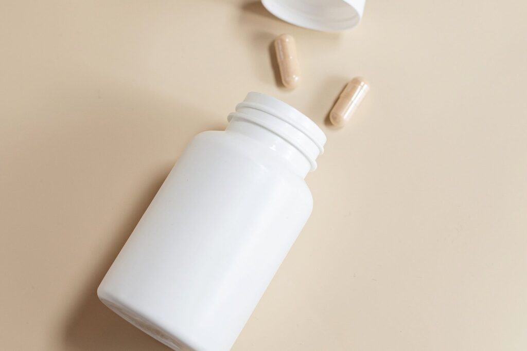 A plain white supplement bottle on its side with two capsules beside it