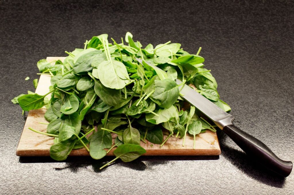 Fresh spinach leaves piled on a wooden cutting board with a knife