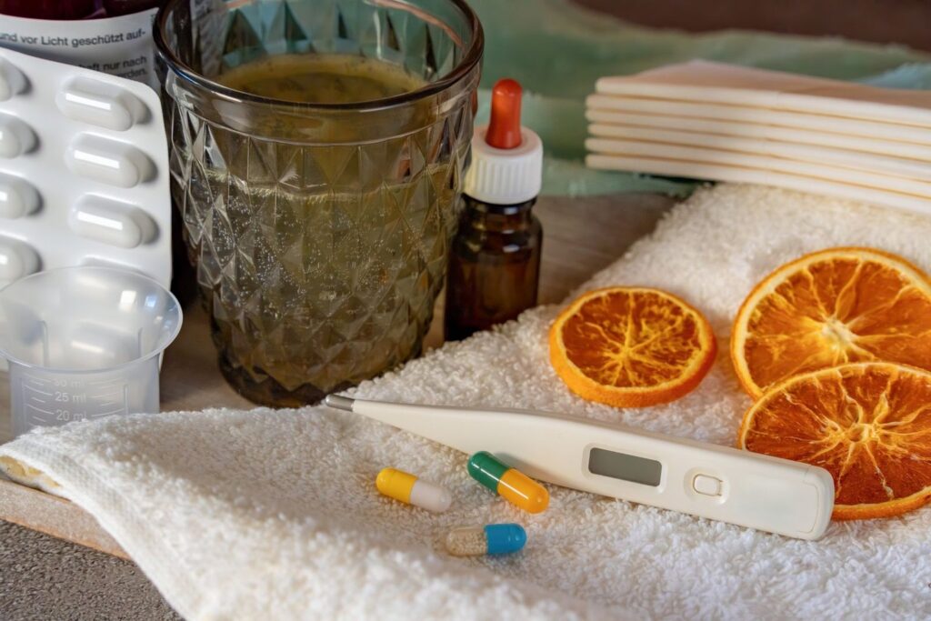 Cold and flu remedies laid out with a thermometer, capsules, dried orange slices and tea