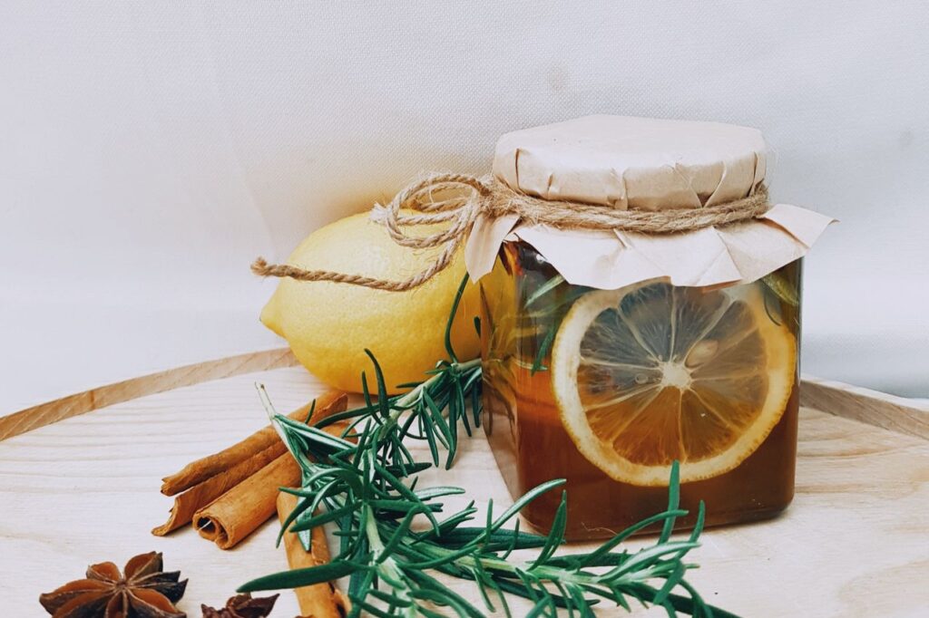 Jar of honey with a lemon slice inside, next to cinnamon sticks, star anise and fresh rosemary on a wooden board
