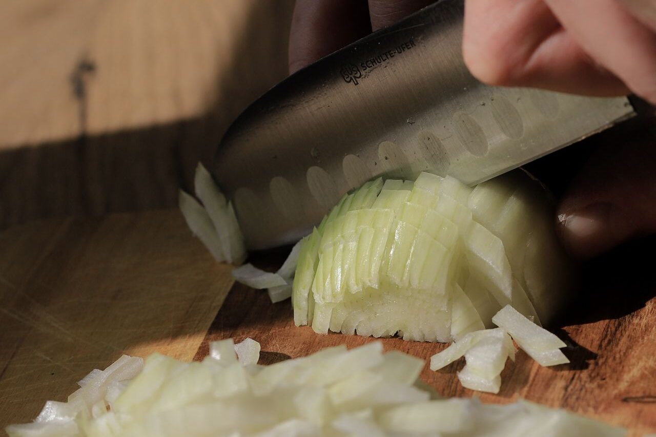 Knife finely chopping a white onion on a wooden board to make onion cough syrup