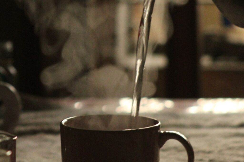 Hot water being poured from a kettle into a mug with steam rising in a warm indoor light