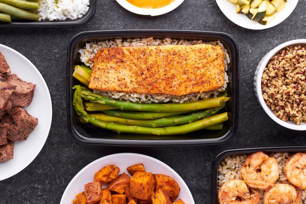Meal prep containers with salmon, asparagus, prawns, sweet potato and grains