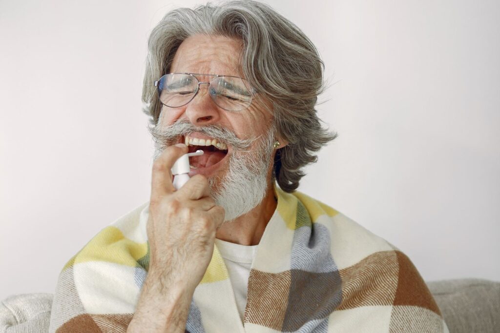 Older man in a checked blanket using a throat spray