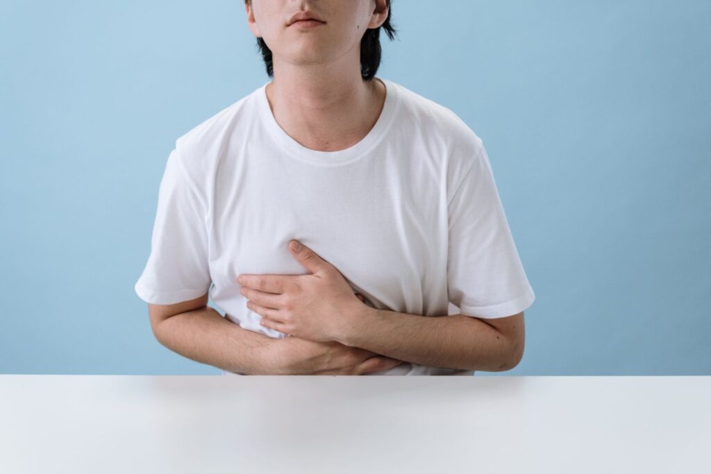 A man in a white shirt holding his stomach in discomfort