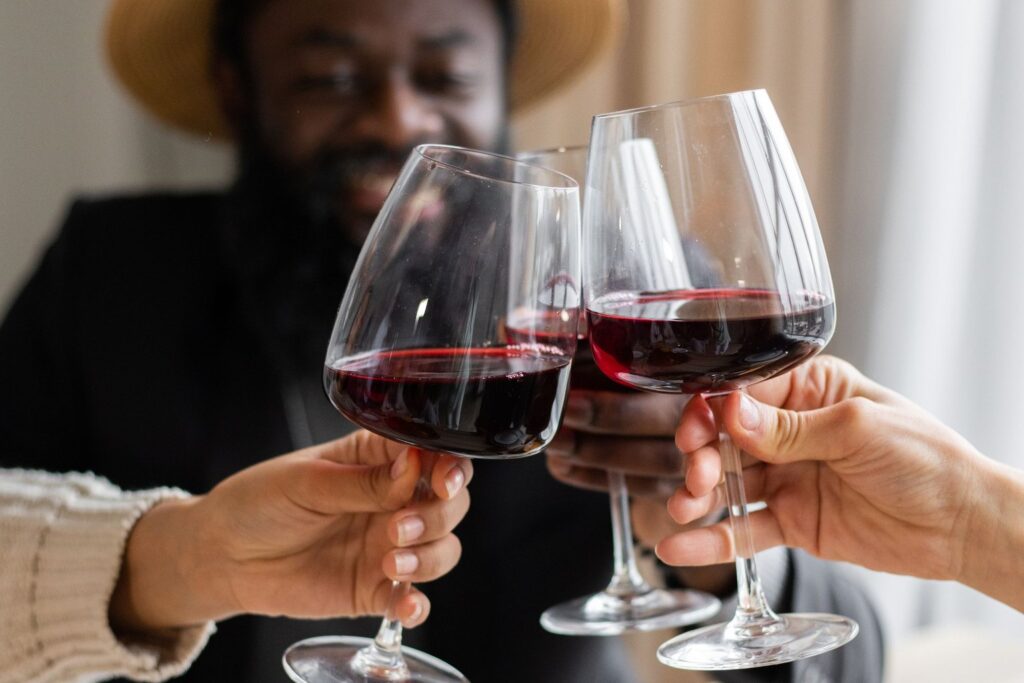 Two people clinking glasses of red wine across a dinner table