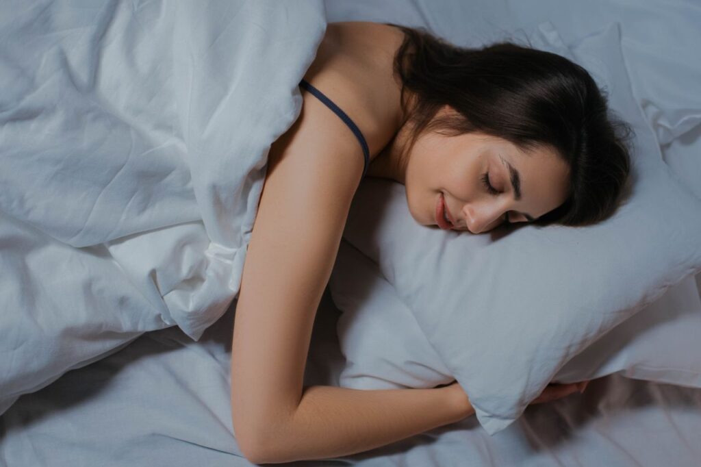 Young woman sleeping in a bed with white linen in soft daylight