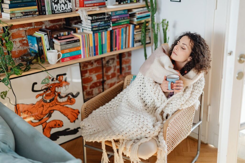 Woman with a cold wrapped in a shawl drinking a warm mug of tea at home