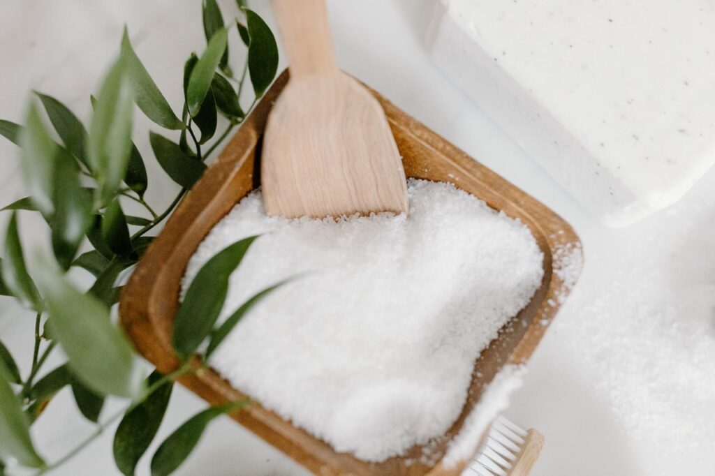 Bath salts in a wooden bowl with a wooden spoon beside a bathtub