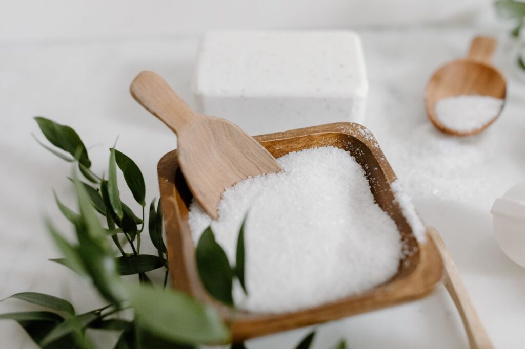 Wooden bowl of fine white non-iodised salt with a small wooden scoop on a marble surface