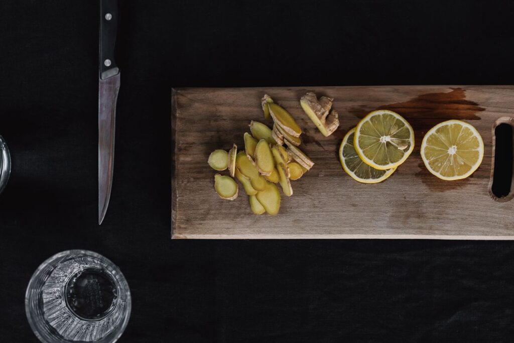 Sliced fresh ginger and lemon rounds on a wooden chopping board, prepped for a fire cider recipe