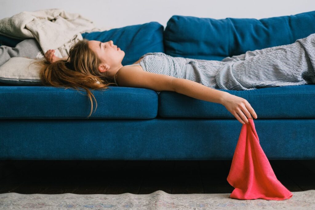 Woman lying exhausted on a blue sofa with one arm hanging down