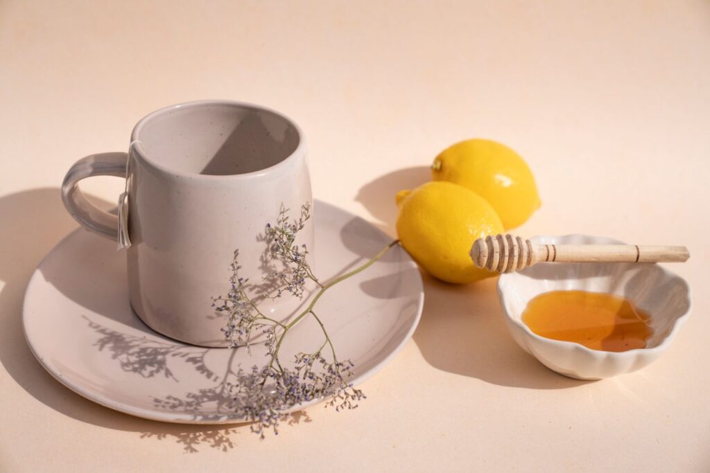 Ceramic mug on a saucer, two fresh lemons and a small bowl of honey with a honey dipper