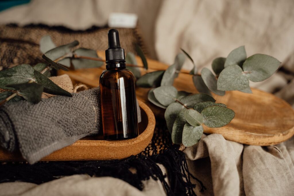 Amber dropper bottle of essential oil on a wooden tray with eucalyptus leaves and a folded towel