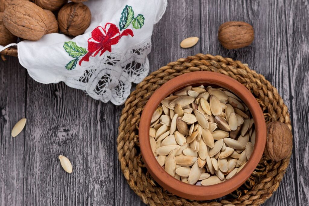 Pumpkin seeds in a terracotta bowl with walnuts on a rustic wooden table