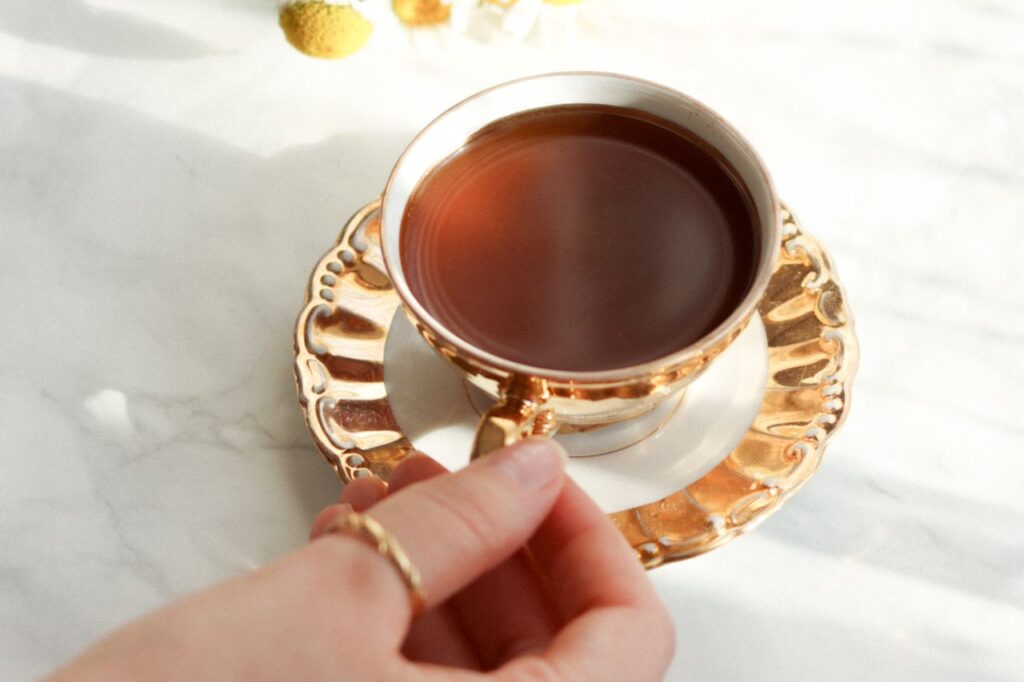 Hand holding a ceramic cup of chamomile tea in sunlight next to a small bouquet of chamomile flowers on a white cloth