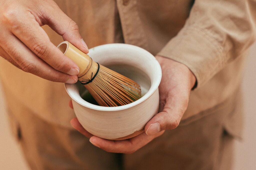 Hands whisking matcha green tea in a ceramic bowl with a bamboo whisk