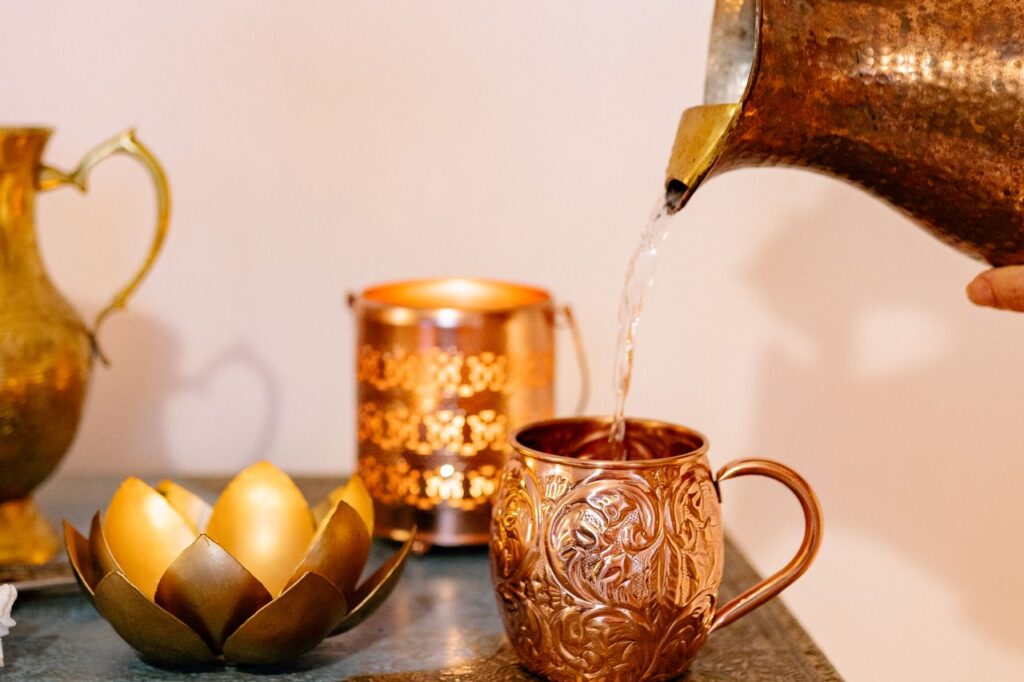 Hand tilting a small brass spouted pot to pour a thin stream of water, the same pouring motion used with a neti pot