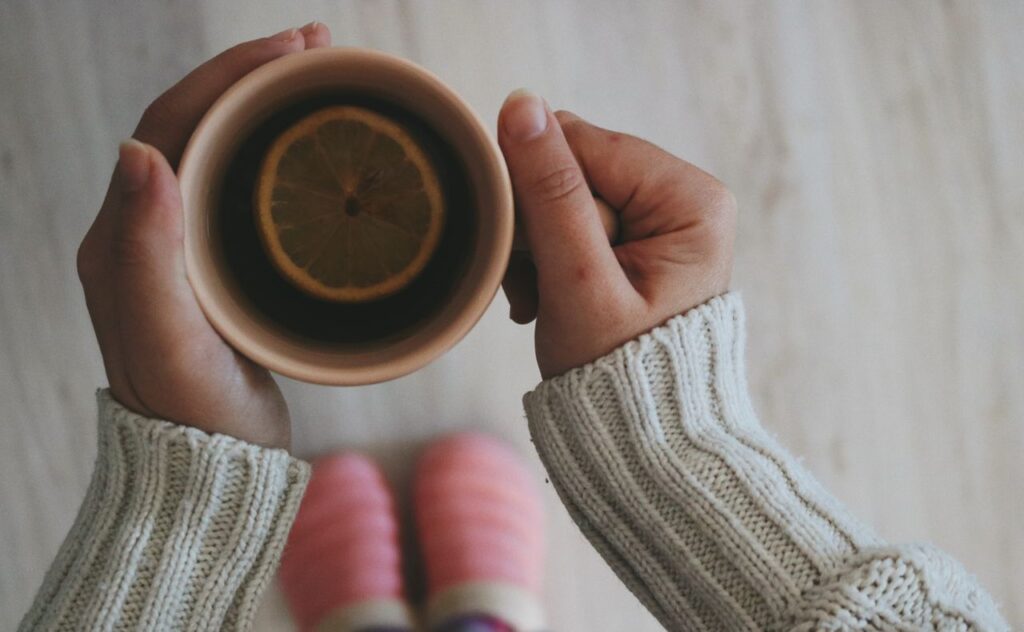 Hands in a cosy knitted jumper holding a cup of tea with a lemon slice, seen from above