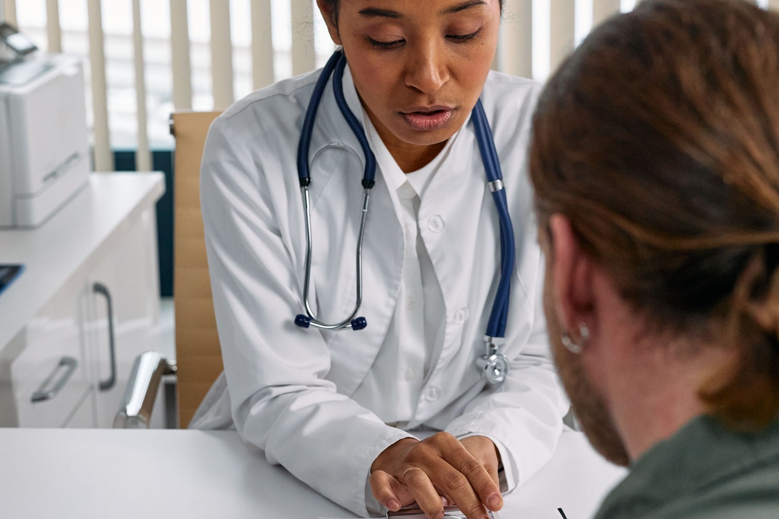 A doctor in a white coat going through a health chart with a patient at a desk