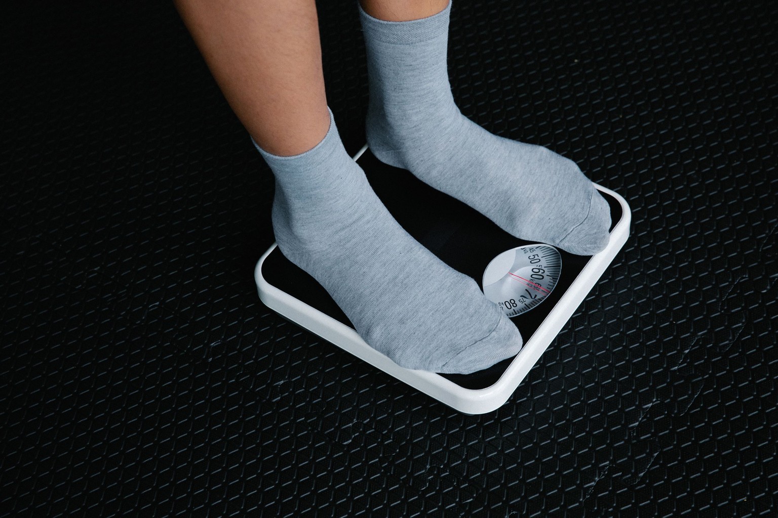 A person in grey socks standing on a white bathroom scale