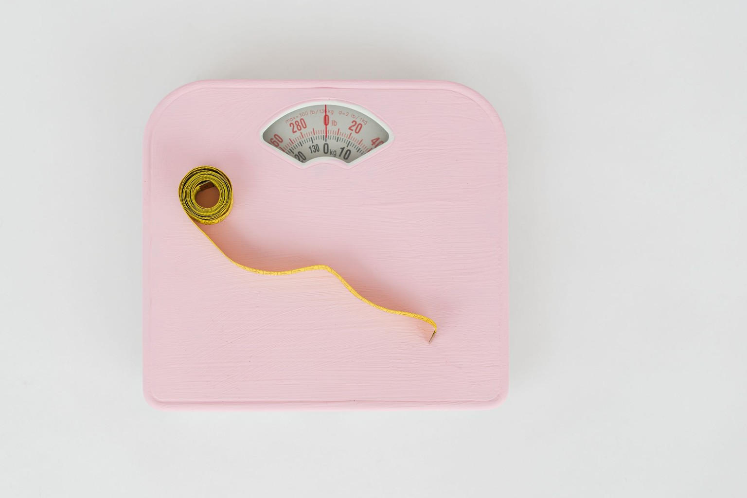 A pink bathroom scale and a yellow tape measure photographed from above on a white background