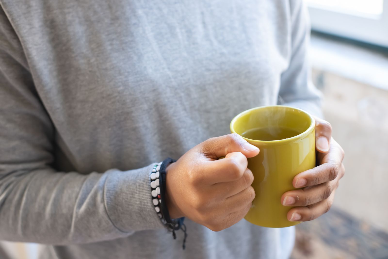 A person in a grey jumper holding a steaming mug of a hot drink