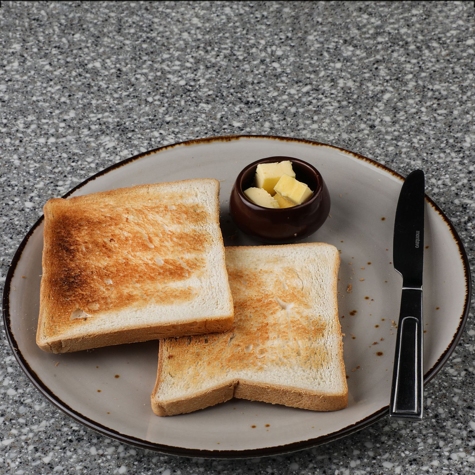 Two slices of toast on a plate with a small pot of butter and a knife