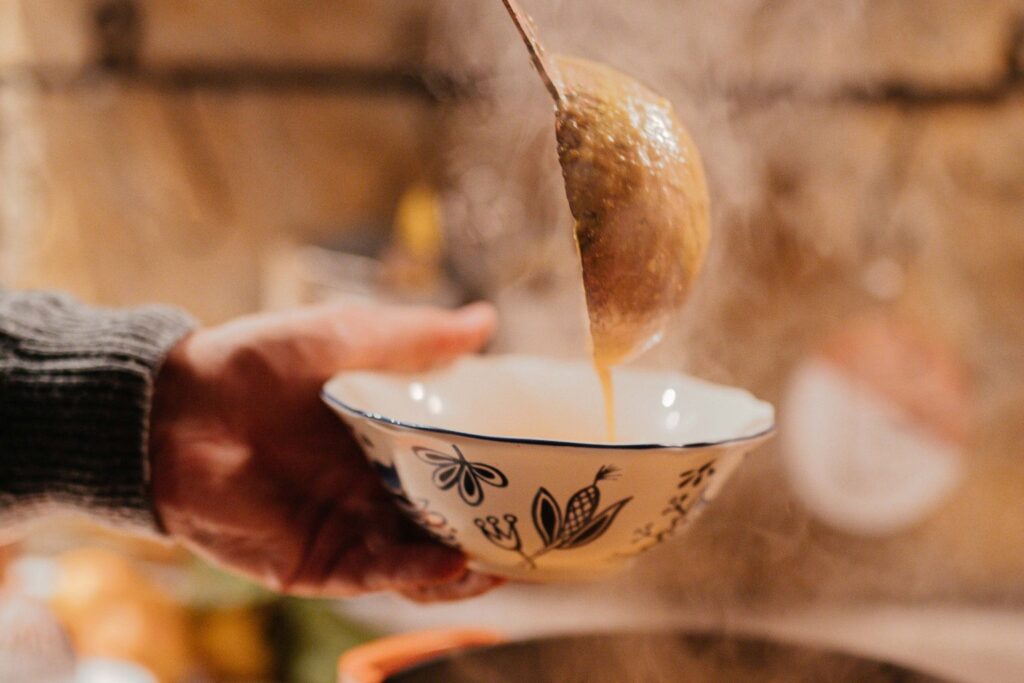 Steaming broth being ladled from a pan into a patterned bowl