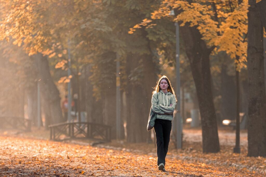 A person walking through a sunlit park on an autumn morning