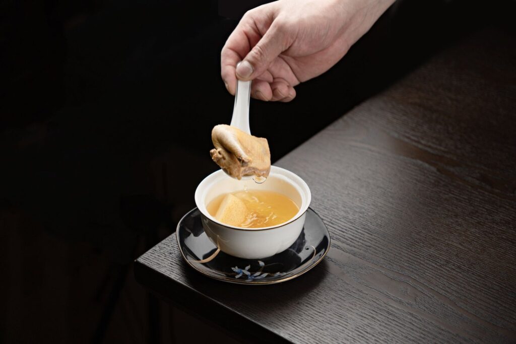 A small cup of clear broth with a spoon resting on a dark table