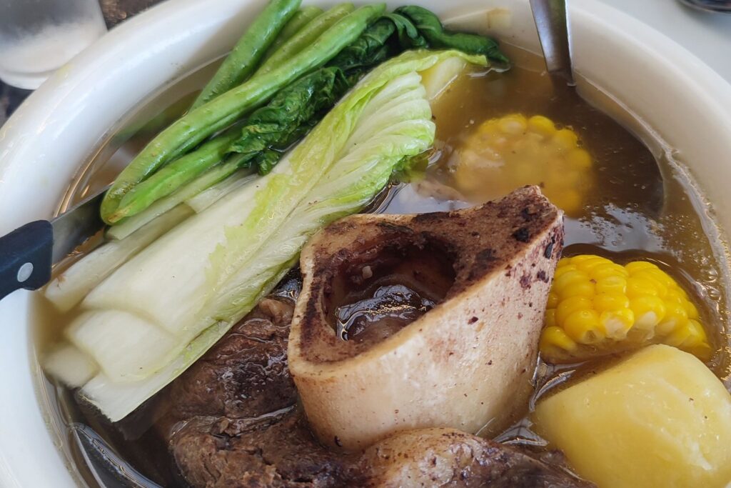 Beef soup with a marrow bone, pak choi, corn and potato in a white bowl