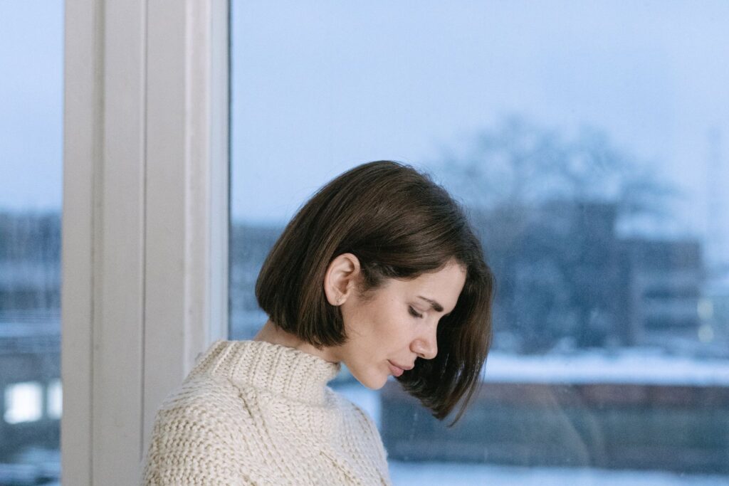 A woman in a knitted jumper looking out of a window on a grey winter day